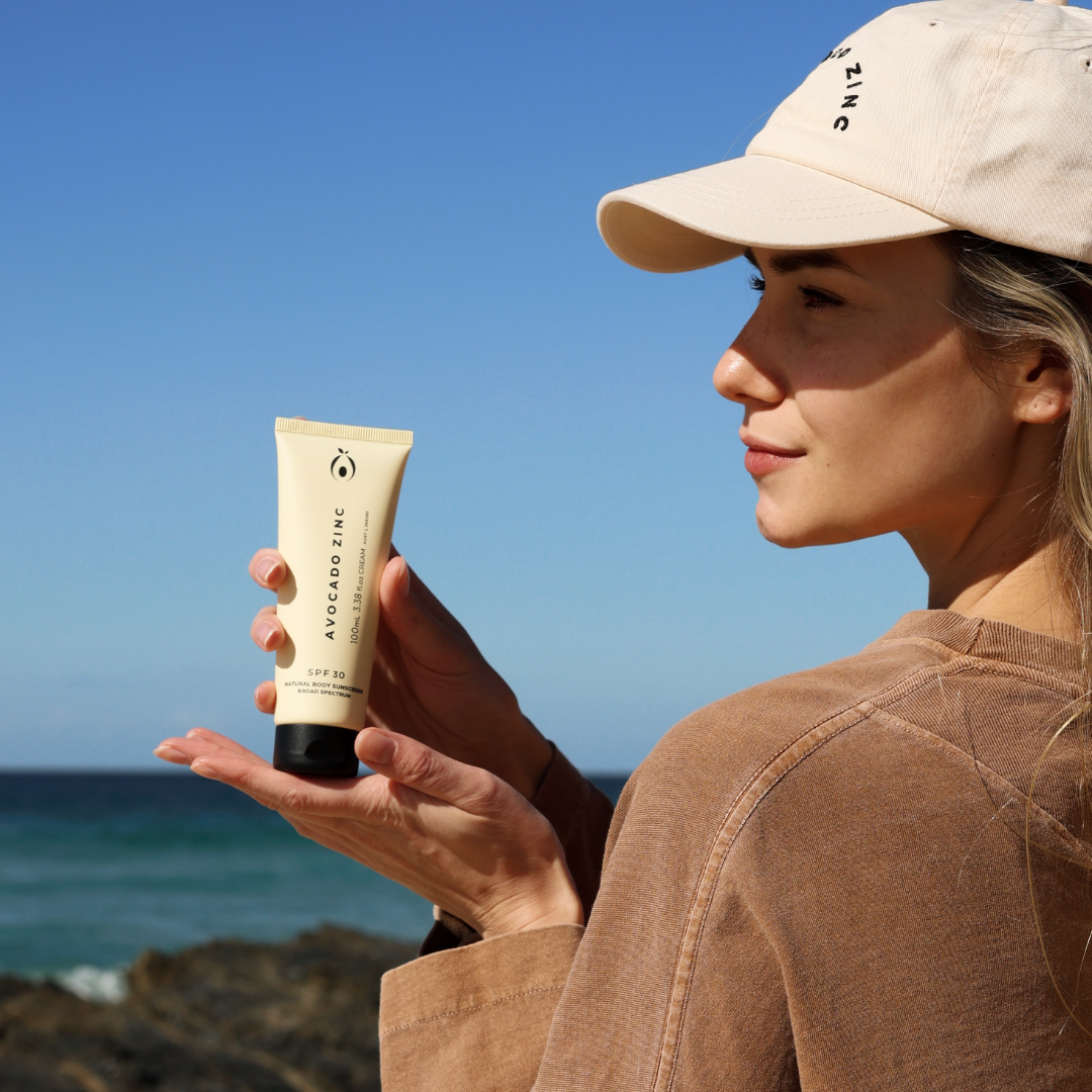 Woman holding SPF 30 Natural Body Sunscreen with ocean in the background, suitable for sensitive, eczema-prone and autoimmune skin.