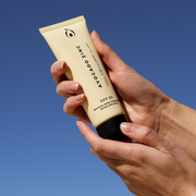 Hands holding SPF 30 Natural Body Sunscreen against a blue sky, highlighting its broad-spectrum sun protection for sensitive and eczema-prone skin.
